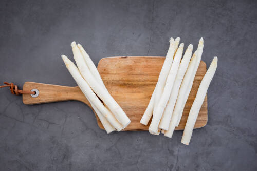 Geschälter Spargel auf Schneidebrett vor dunklem Hintergrund.