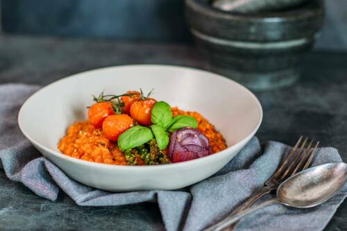 Spargelrisotto mit Tomaten in Teller vor dunklem Hintergrund.