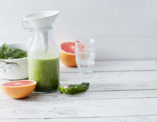 Spinat-Grapefruit-Smoothie in Glas neben aufgeschnittener Grapefruit vor hellem Hintergrund.