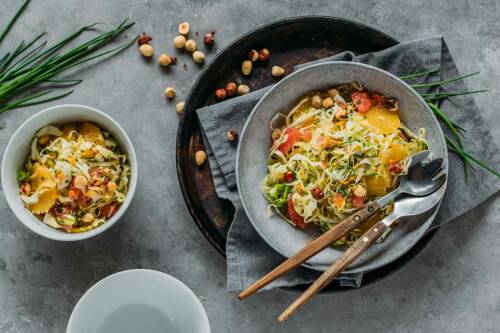 Spitzkohlsalat in Teller und Schüssel neben Schnittlauch vor hellem Hintergrund.
