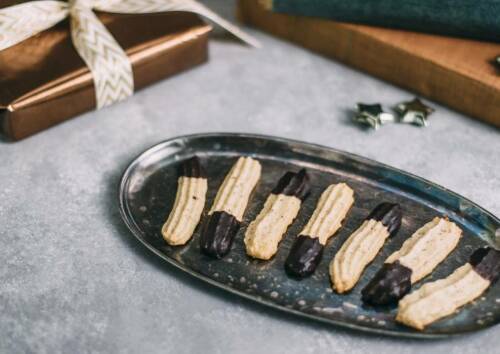Längliches Spritzgebäck mit Schokoüberzug auf einer Platte, von oben fotografiert.