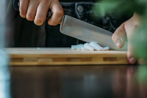 Schneidebrett, auf dem gerade ein Stück Kernseife mit einem Messer zerkleinert wird.