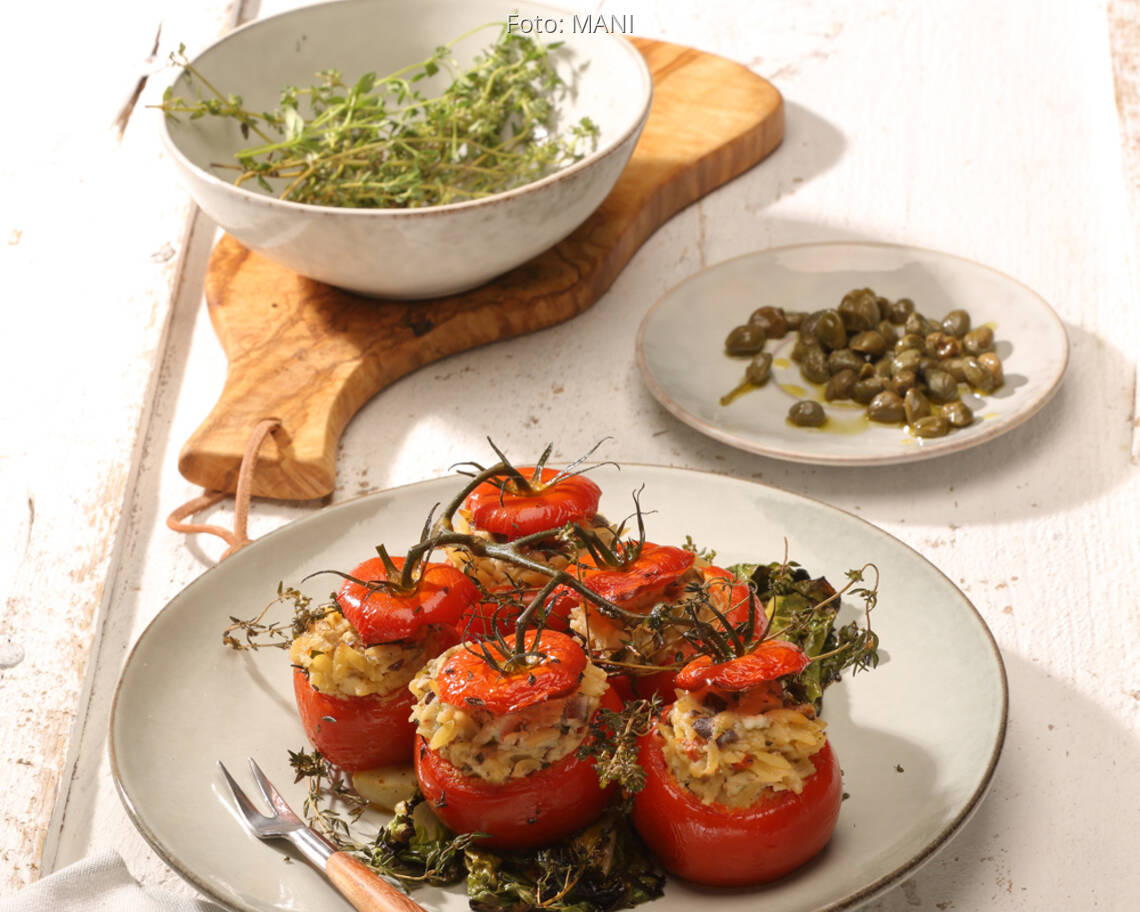 Gefüllte Tomaten auf weißem Teller mit Salat und Kapern auf kleinem Teller
