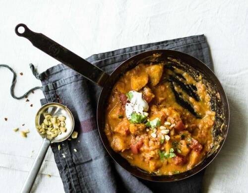 Süßkartoffeln in scharfer Soße mit Creme fraiche in gusseiserner Pfanne vor hellem Hintegrund.
