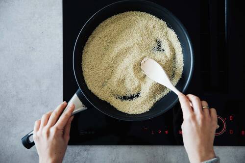 Sesamsamen in Pfanne rösten mit Kochlöffel und Händen.