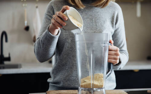 Sesampaste in Mixer mit Händen vor hellem Hintergrund.