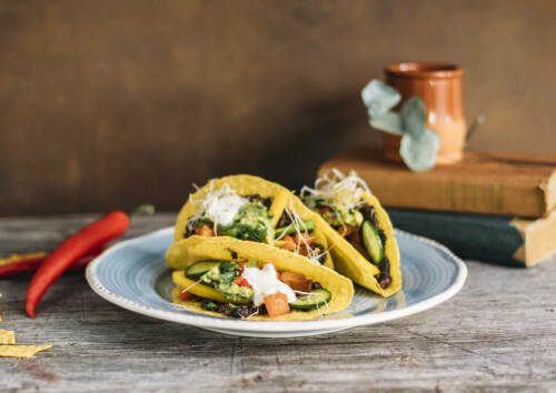 Wenn man mexikanisch Essen geht, dann dürfen Tacos natürlich nicht fehlen. Diese hier kommen in einer veganen Variante daher. Drei gefüllte Tacos auf einem Teller, von vorne fotografiert.