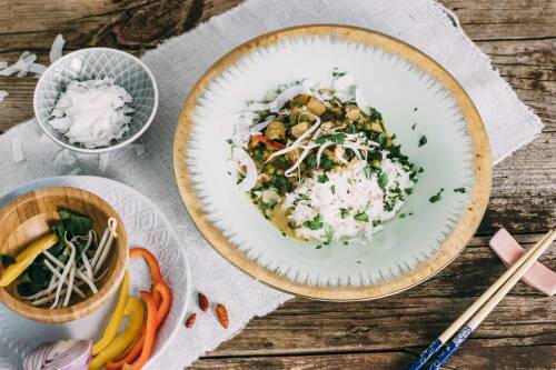 buntes Thai-Curry mit Reis in einer Schüssel, daneben Stäbchen und verschiedenes Gemüse: Paprika, Sprossen und Schalotten, von oben fotografiert