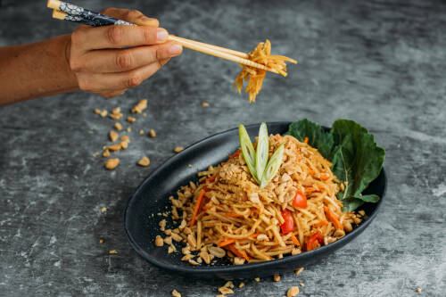 Eine Hand fischt mit Stäbchen etwas von einem Teller Thai-Peanut-Salad.