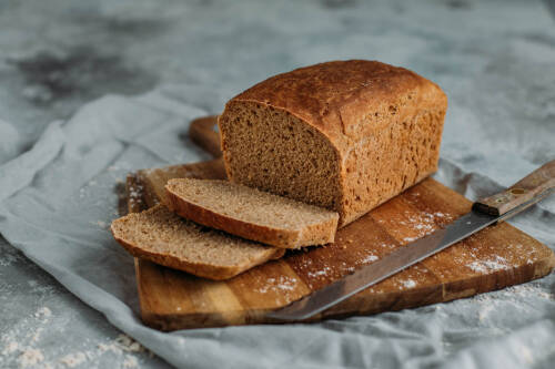 Ein frisch gebackenes Urkornbrot: Es liegt aufgeschnitten auf einem Holzbrett, mit zwei Brotscheiben davor.