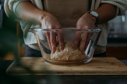 Die Zutaten für Urkornbrot werden in einer gläsernen Schüssel zu einem homogenen Teig geknetet.