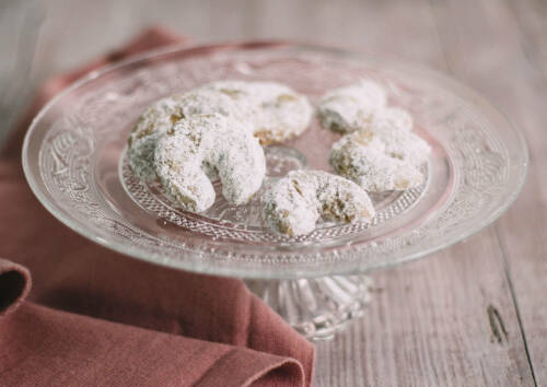 Ein Klassiker unter den Plätzchen: Die gebogenen Vanillekipferl auf einer Platte angerichtet und mit Vanille-Puderzucker bestäubt. Von oben fotografiert.