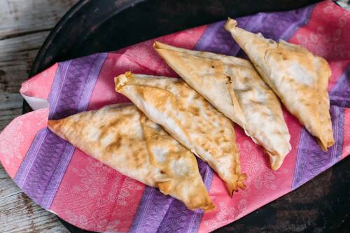 Vegane Blumenkohlreis Samosas auf bunten Servietten vor dunklem Hintergrund.