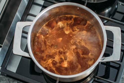 Vegane Bratensoße in Topf kochend vor dunklem Hintergrund.