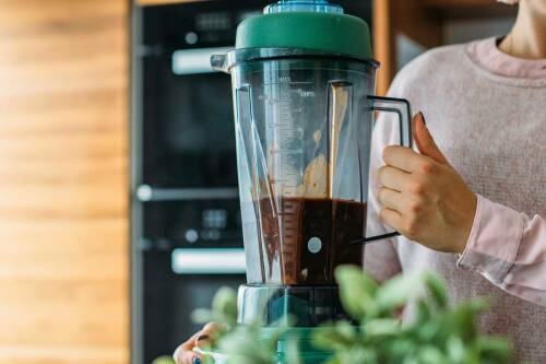 Vegane Bratensoße in Mixer mit Händen vor hellem Hintergrund.