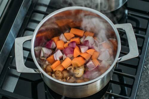 Vegane Bratensoße mit Gemüse in Topf vor dunklem Hintergrund.