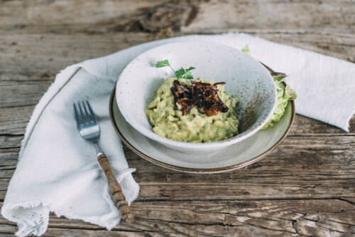 Selbst gemachte vegane Käsespätzle: Mit Röstzwiebeln in einer hellen Schüssel auf dem rustikalen Holztisch