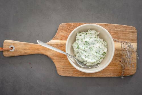 Vegane Kräuterbutter in Schüssel auf Schneidebrett vor dunklem Hintergrund.