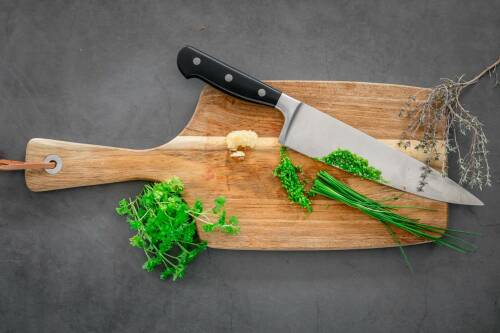 Vegane Kräuterbutter auf Schneidebrett mit Kräutern und Messern vor dunklem Hintergrund.