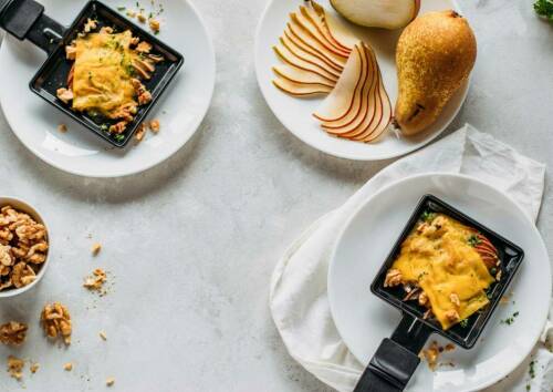 Zwei fertige Raclette-Pfännchen mit Birne, Walnuss und veganer Käsealternative.