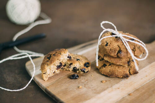 Vegane Schokokekse mit Cranberries auf Schneidebrett vor dunklem Hintergrund.
