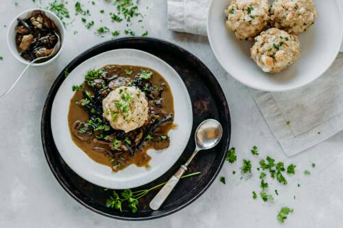 Vegane Semmelknödel mit Waldpilzrahmsoße auf weißem Teller vor hellem Hintergrund.