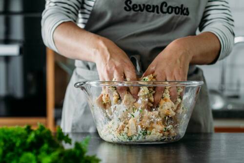 Semmelknödelteig in Schüssel mit Händen vermengt vor hellem Hintergrund.