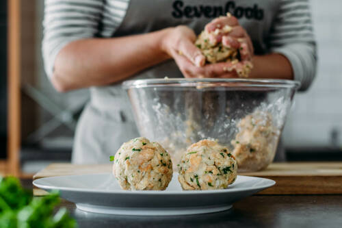 Semmelknödel mit Händen geformt über Schüssel und Teller vor hellem Hintergrund.