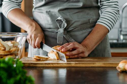 Brot schneiden mit Brotmesser auf Schneidebrett vor hellem Hintergrund.