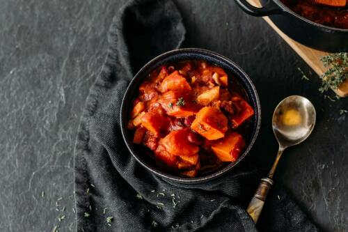 Veganer Kürbis-Bohnen-Eintopf in schwarzem Teller vor dunklem Hintergrund.