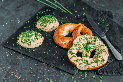 Veganer Obazda auf einer Brezen mit Schnittlauch bestreut.