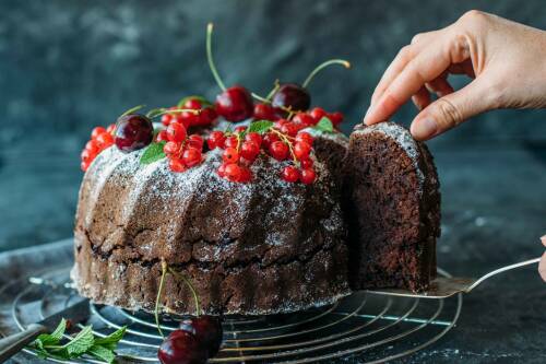 Veganer Schokokuchen mit Johannisbeeren und Hand vor dunklem Hintergrund.