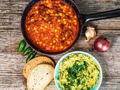 veganes Karottenchili neben Guacamole und Brotscheiben vor dunklem Hintergrund.
