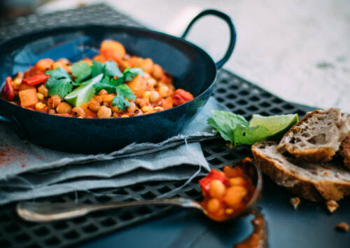 Vielleicht nicht typisch mexikanisch, aber auf jeden Fall ein tolles Essen, ist dieses vegane Kichererbsen-Chili. Hier in einem schwarzen Pfännchen auf einem Gitter, daneben eine Schöpfkelle, von der Seite fotografiert.