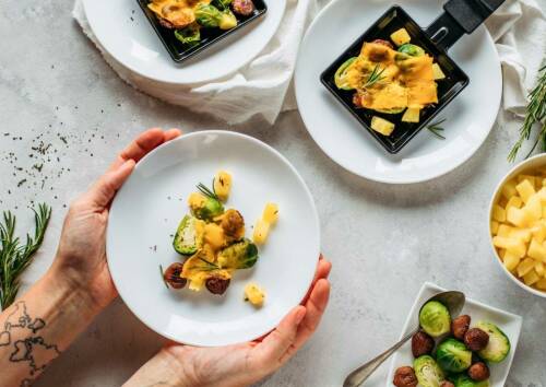 Leckeres veganes Raclette-Pfännchen mit Wintergemüse auf einem weißen Teller.