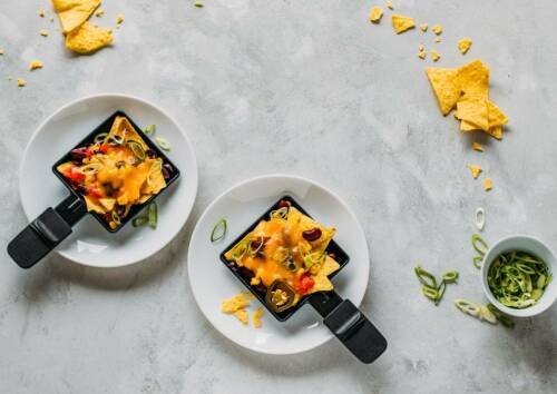 Zwei fertige Raclette-Pfännchen mit Nachos und Bohnen mit Käse überbacken.