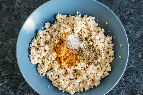 Zerbröseltes Tofu in Schüssel mit Gewürzen.