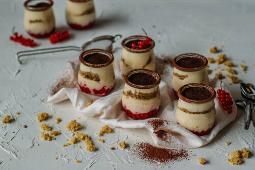 Veganes Tiramisu in Gläsern mit Johannisbeeren vor hellem Hintergrund.