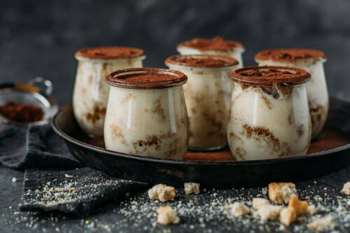 Fünf Gläser Veganes Tiramisu auf einem Tablett.