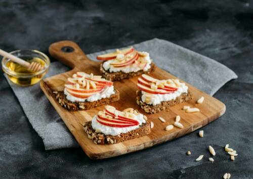 Scheiben Brot mit Apfel Hüttenkäse und Mandelsplitter auf einem Brett