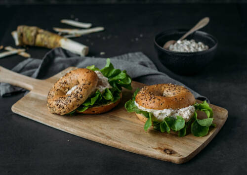 Frisch belegter Bagel mit Apfel-Meerrettich-Aufstrich auf einem Holzbrett.