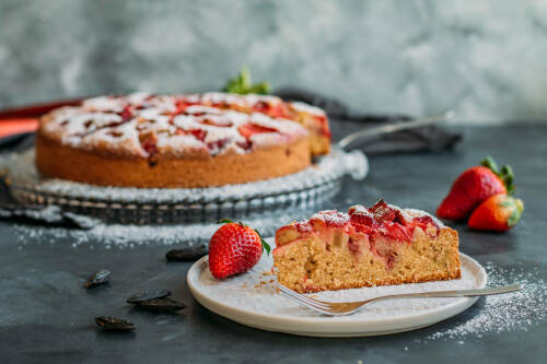 erdbeer rhabarber kuchen angeschnitten auf einem Teller mit Erdbeeren und einer Kuchengabel