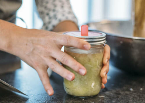 Ein Deckel wird auf ein Glas mit angesetztem Sauerkraut gedreht.
