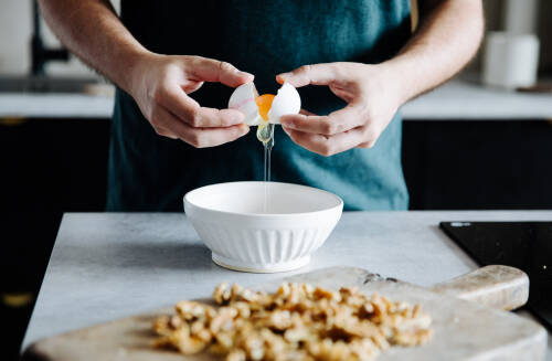 Ein Ei wird über einer weißen Schüssel aufgebrochen, um das Eiweiß zu trennen.