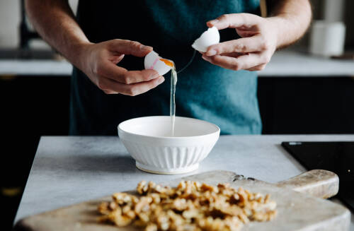 Eier werden über einer Schüssel getrennt und das Eiweiß wird darin aufgefangen.