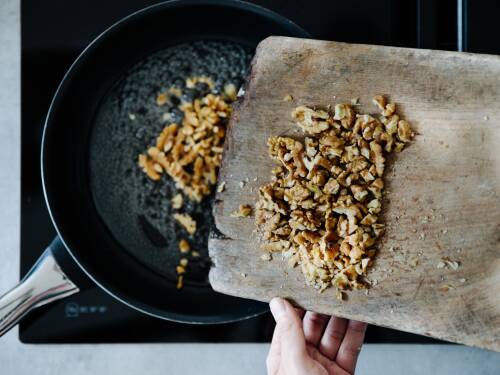 Gehackte Walnüsse werden zum Karamellisieren in eine Pfanne mit heißem Zuckerwasser gegeben.