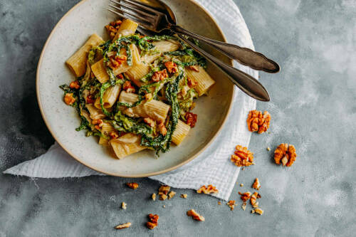 Walnuss-Wirsing-Pfanne mit Rigatoni und Walnüssen vor hellem Hintergrund.