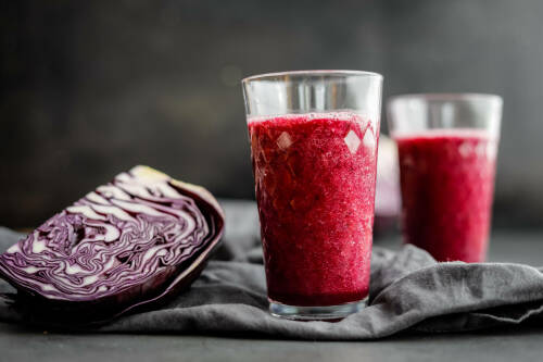 Köstlicher roter Winter-Smoothie in Gläser, daneben geviertelter Rotkohl.