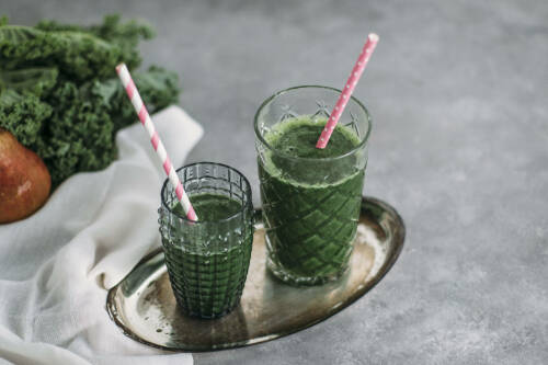 Wintersmoothie aus Grünkohl in Gläsern mit Strohhalmen vor hellem Hintergrund.