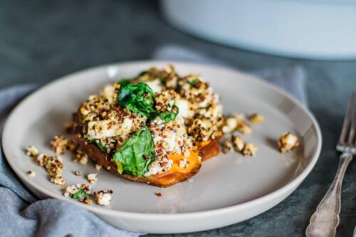 Ofensüßkartoffel mit Quinoa, Feta und Spinat auf einem Teller von der Seite fotografiert.